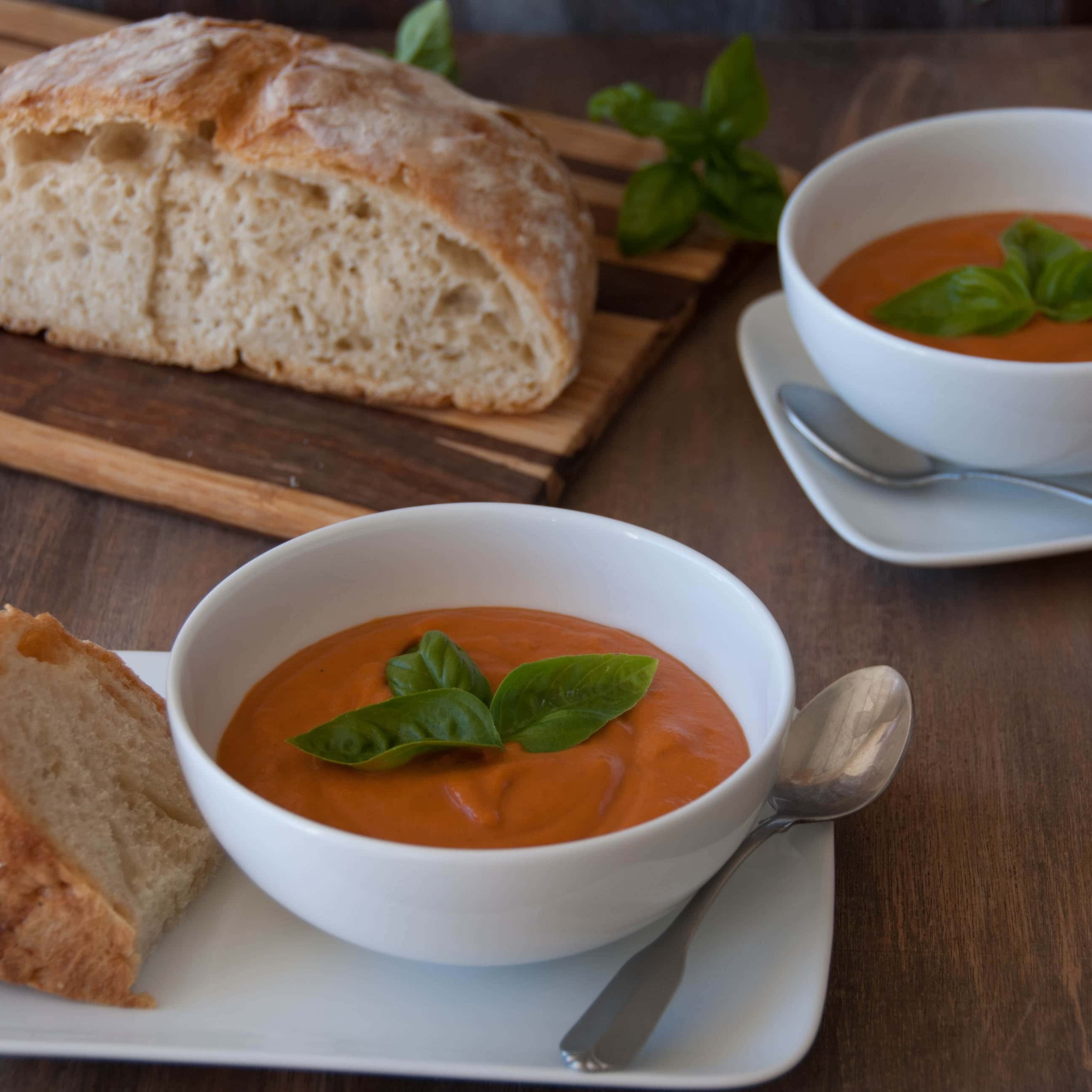 Rich creamy tomato soup in a rustic bowl with crusty bread for dipping, cozy setting