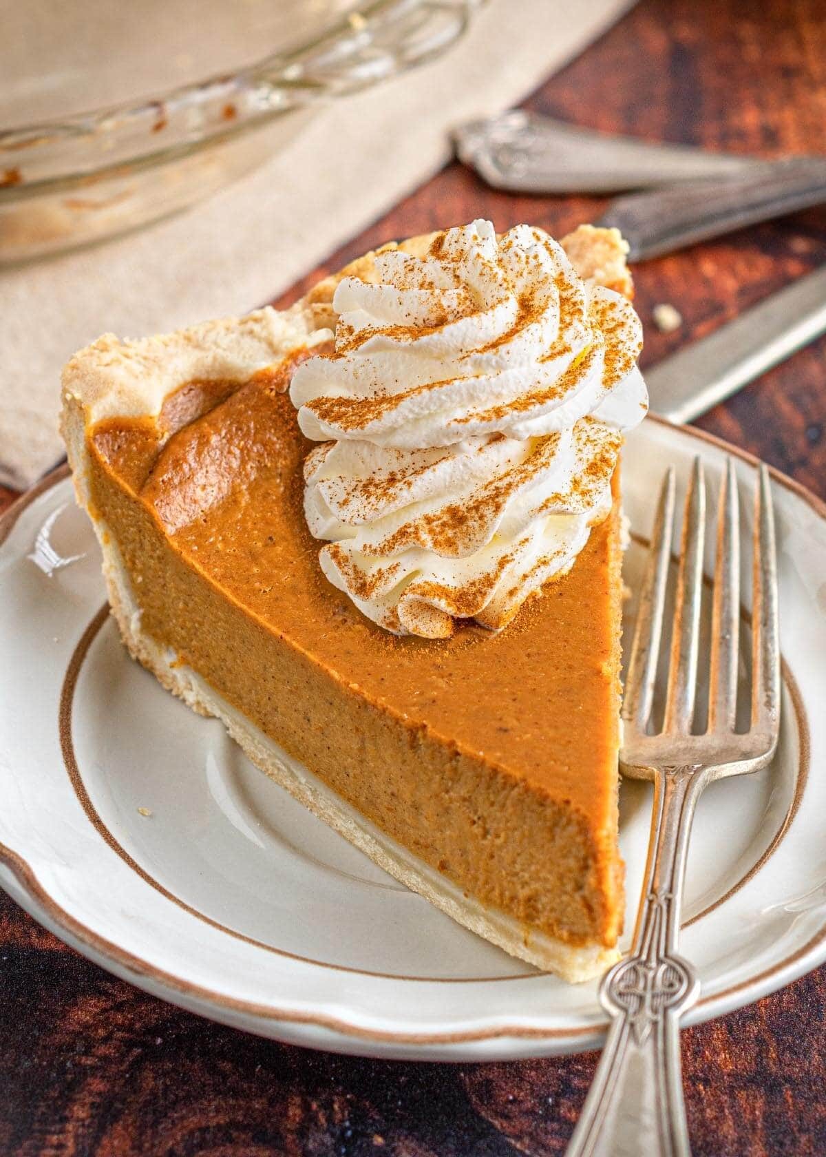 homemade velvety vanilla pumpkin pie with whipped cream topping and a rustic fall background