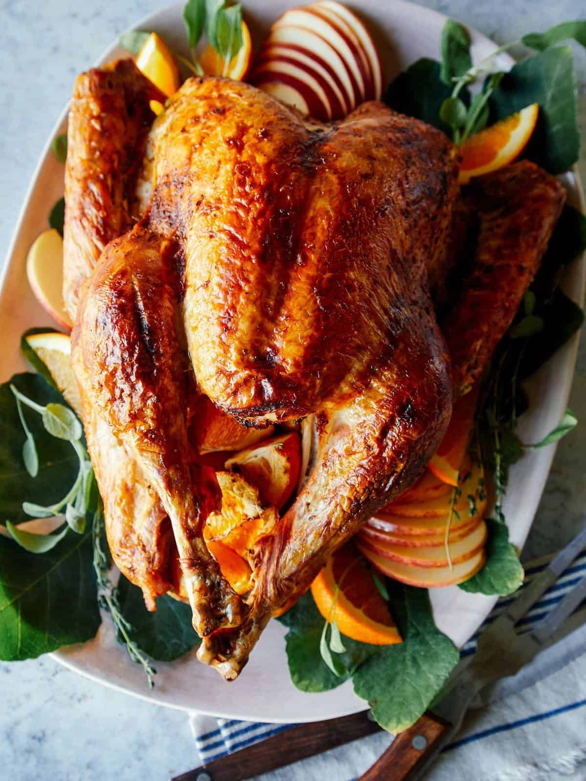 whole roasted golden brown citrus brined turkey on a rustic wooden table with fall decorations