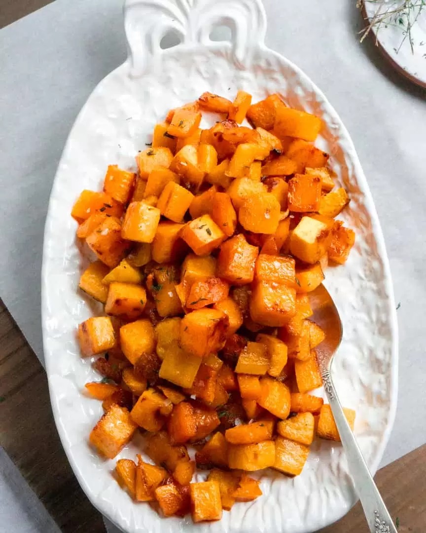 Vibrant roasted butternut squash cubes glazed with maple caramel, arranged on a rustic wooden board, garnished with fresh thyme, warm autumn light