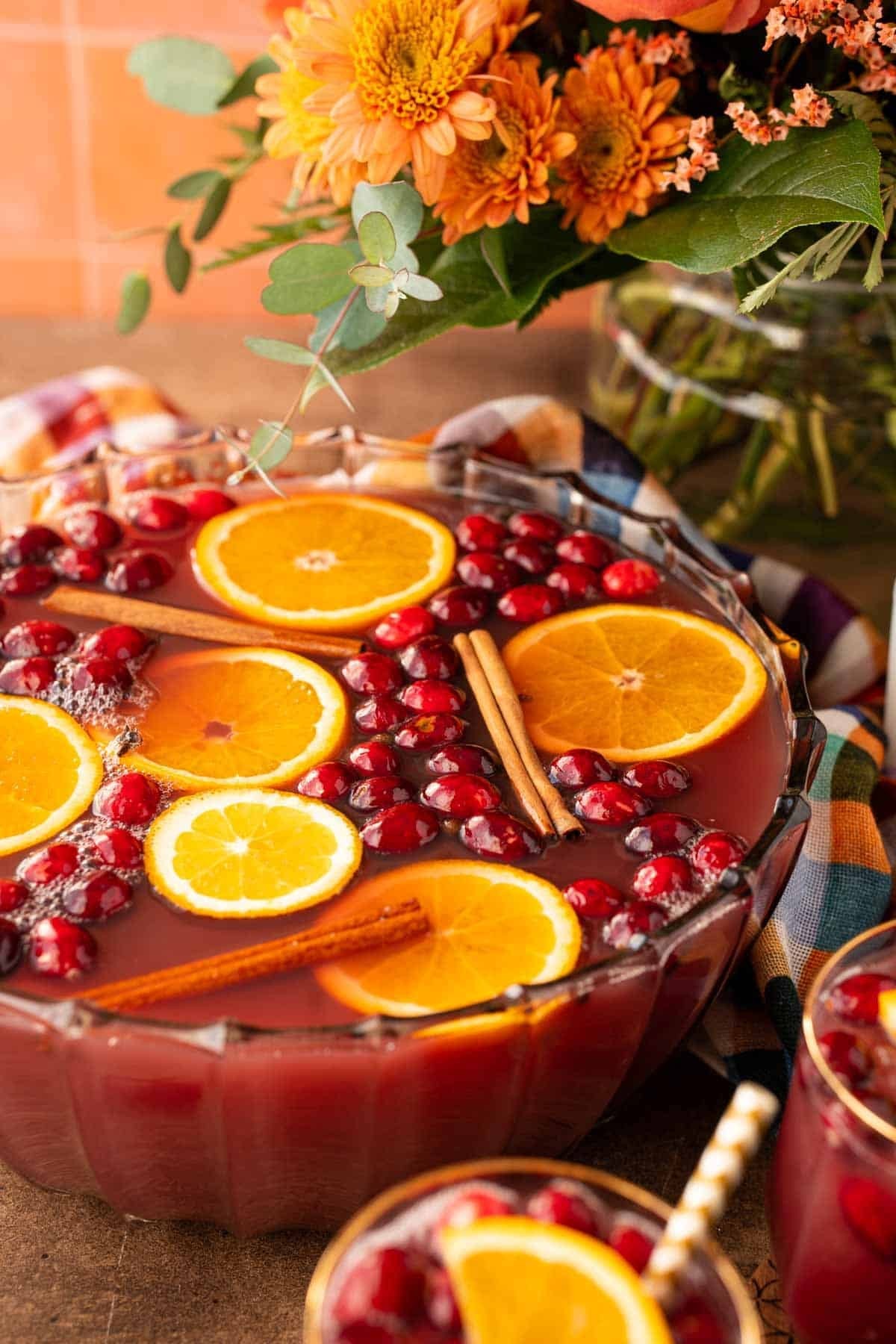 Cozy holiday scene with a steaming punch bowl, garnished with orange slices and cloves, warm lighting