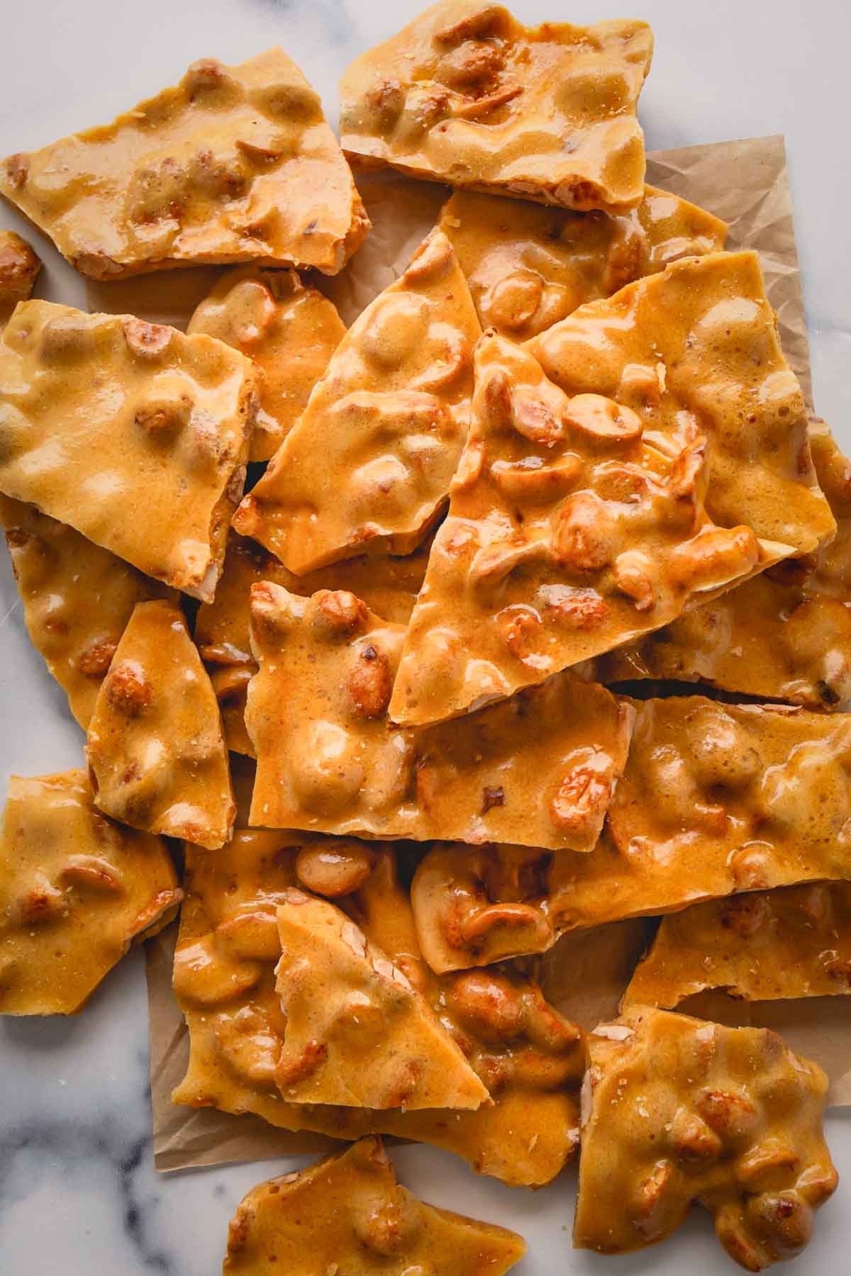 Close-up of golden peanut brittle with a glossy, crunchy texture, broken into pieces on parchment paper