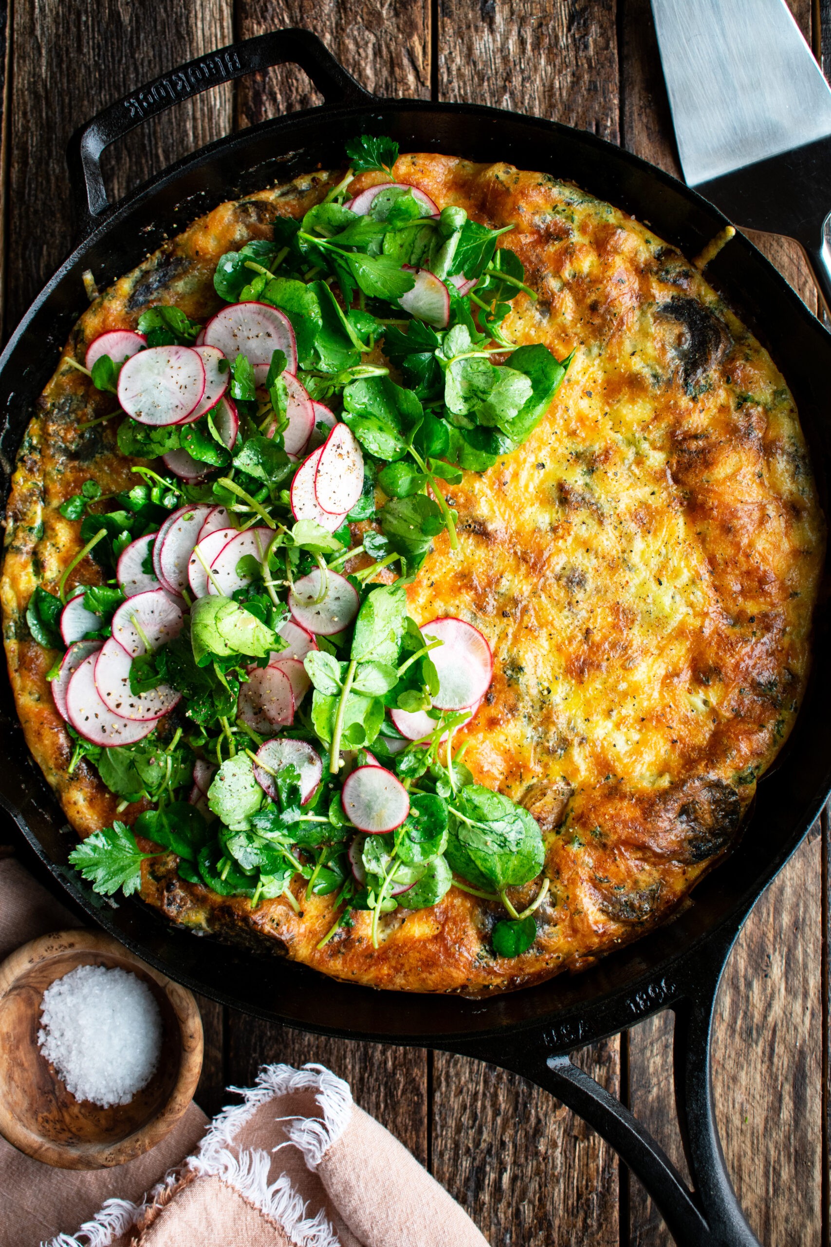 A rustic, golden-brown Gruyere and vegetable frittata in a cast iron skillet, garnished with fresh herbs.