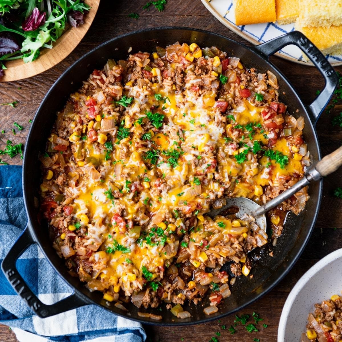 Overhead view of a sizzling ground beef ranch skillet with melted cheddar cheese and fresh green onions, rustic kitchen setting