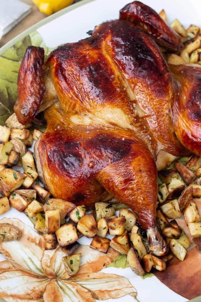 A whole roasted chicken on a platter, garnished with fresh sage sprigs.