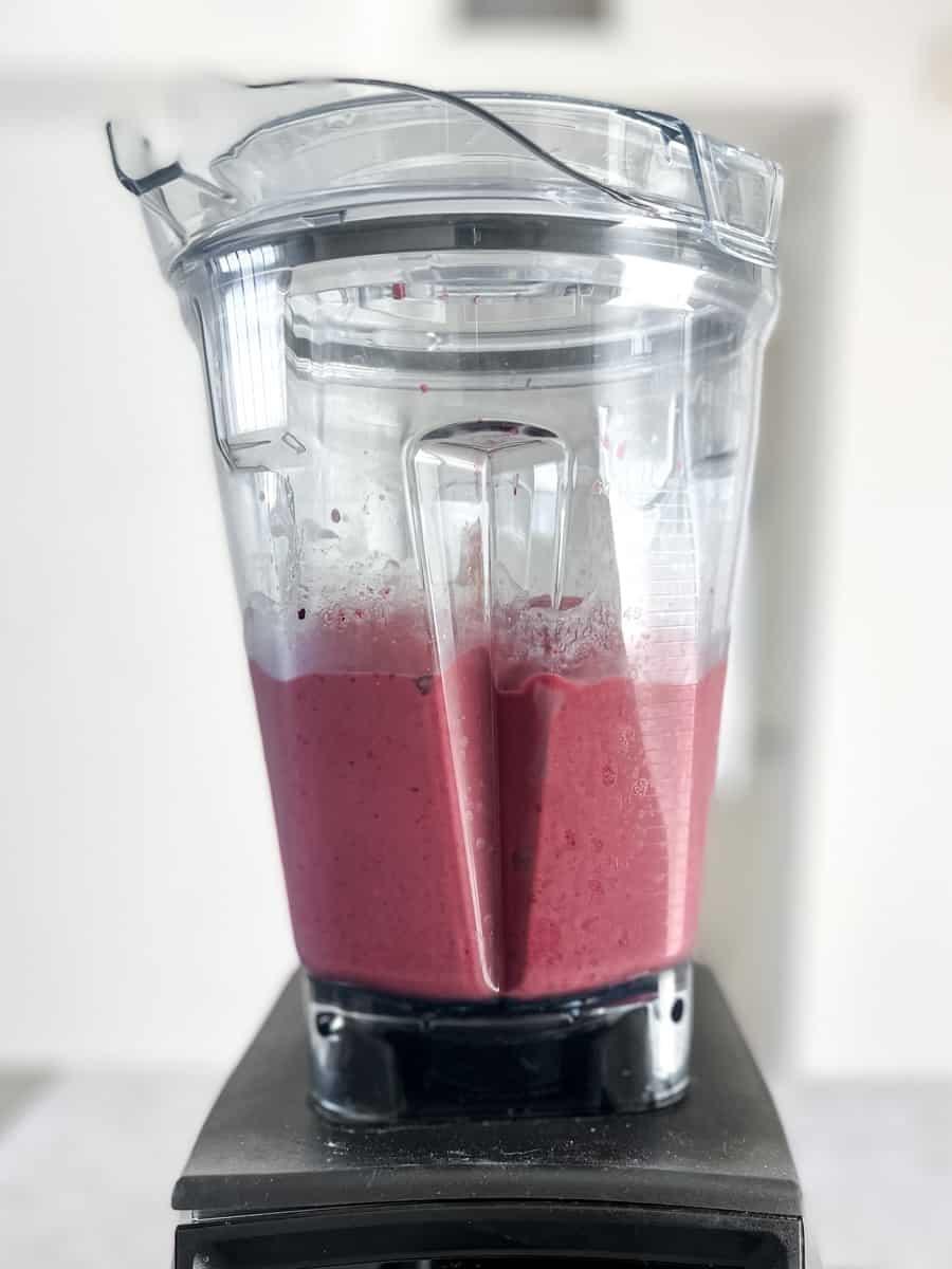 overhead shot of a blender blending a berry smoothie with allspice on the side