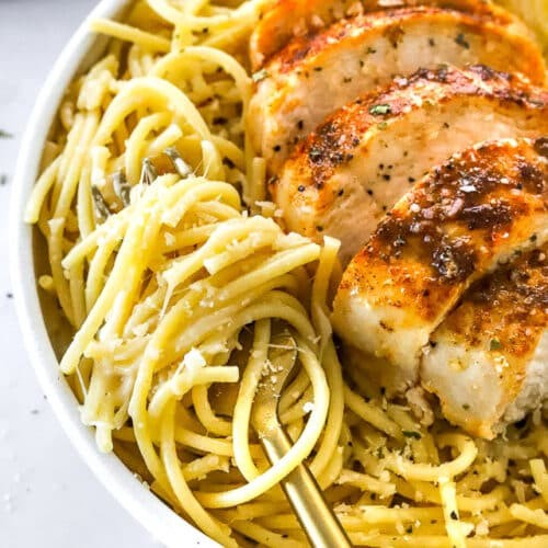 Close-up of golden brown garlic parmesan chicken breast bake, garnished with fresh parsley and a side of pasta