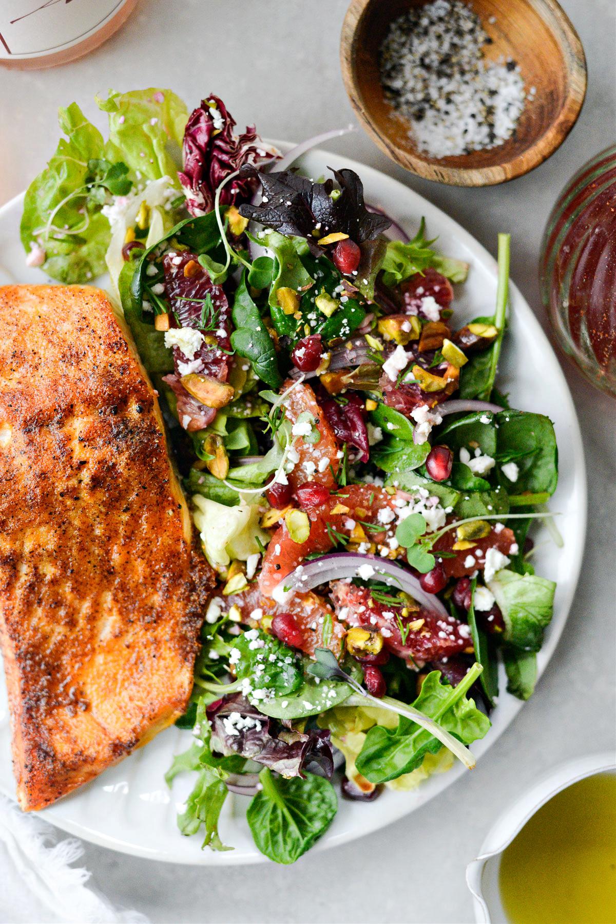 A person tossing a Blood Orange & Pistachio Fattoush salad in a large bowl.