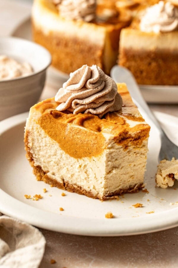 Homemade pumpkin cheesecake with a visible cream cheese swirl, garnished with whipped cream and a sprinkle of cinnamon, cozy autumn background